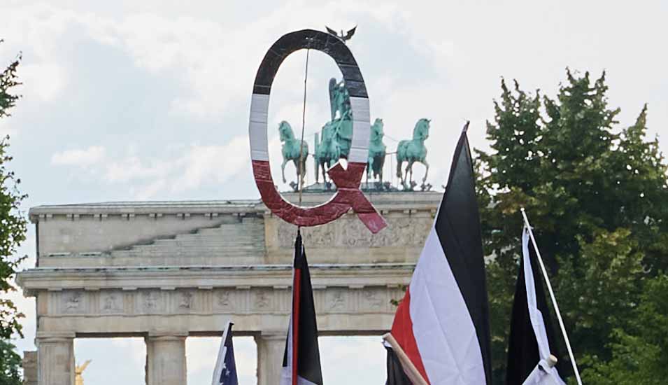 Reichsflaggen und ein Q in den selben Farben halten Demonstranten vor dem Brandenburger Tor. Q steht für QAnon. 