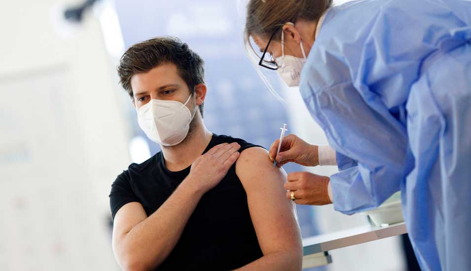 Ärztin impft jungen Mann gegen Covid-19 mit einer Spritze in den Oberarm