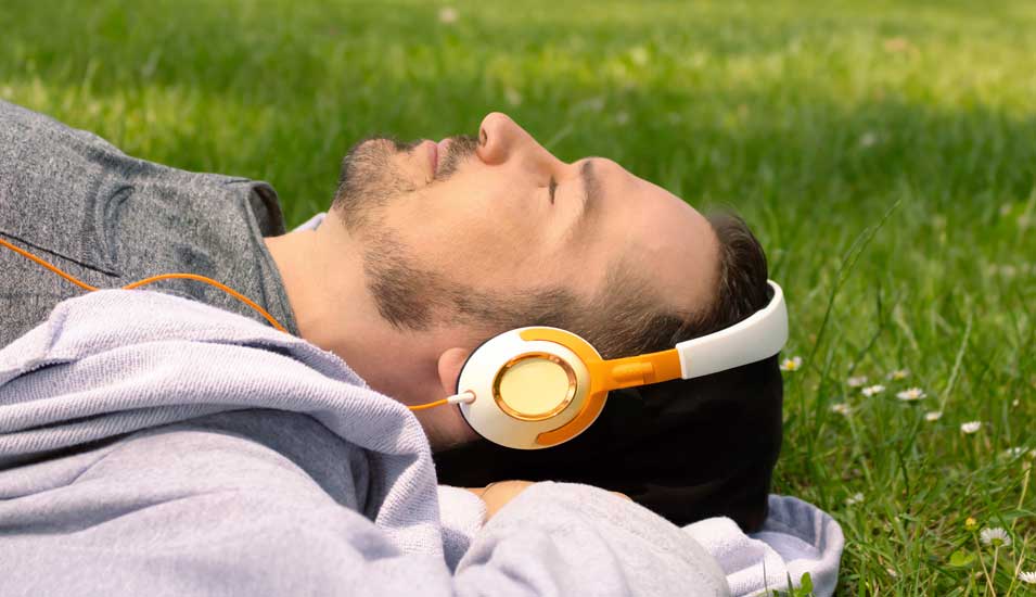 Mann liegt mit Kopfhörern im Gras und entspannt. 