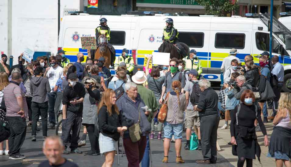 Migrationsgegner und Migrationsbefürworter stoßen bei Protesten in Dover, England aufeinander, im Bildhintergrund stehen Polizisten.