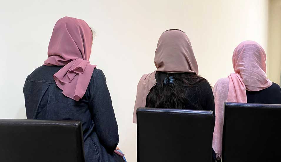 Drei Frauen mit Kopftüchern sitzen mit dem Rücken zum Fotografen, man erkennt ihre Gesichter nicht.