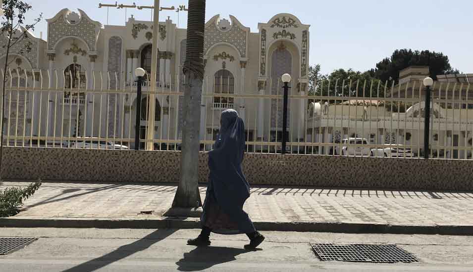 Eine Frau geht eine Straße in Kabul entlang. Sie trägt ein langes Gewand mit Kopftuch und Gesichtsschleier.