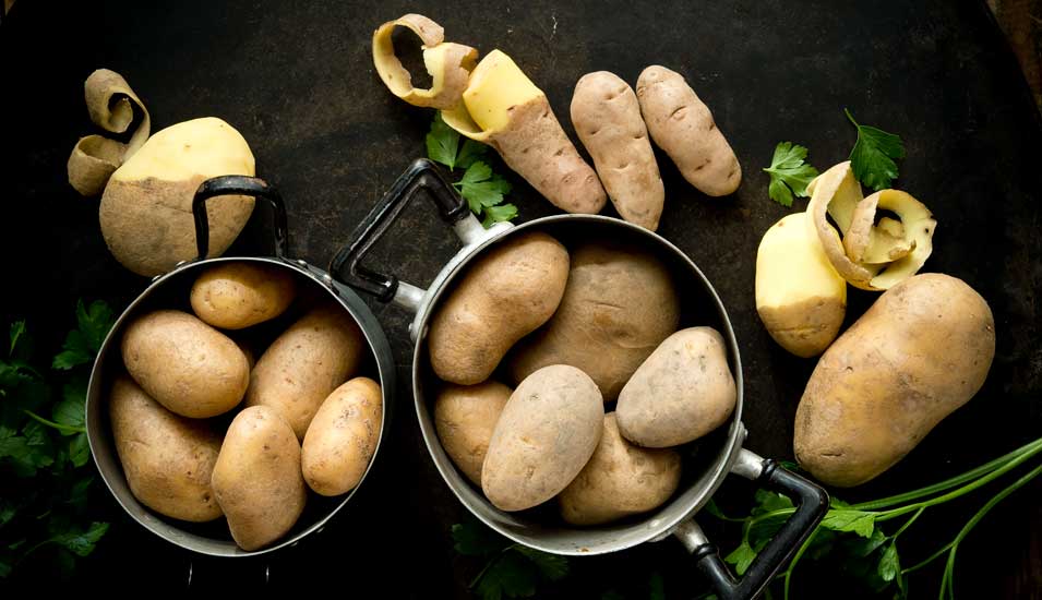 Töpfe mit unterschiedlichen Kartoffelsorten, geschält und ungeschält.