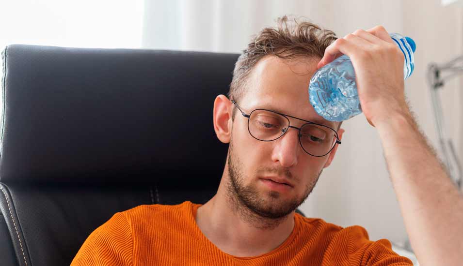 Unter Hitze leidender Mann kühlt seine Stirn mit einer Wasserflasche