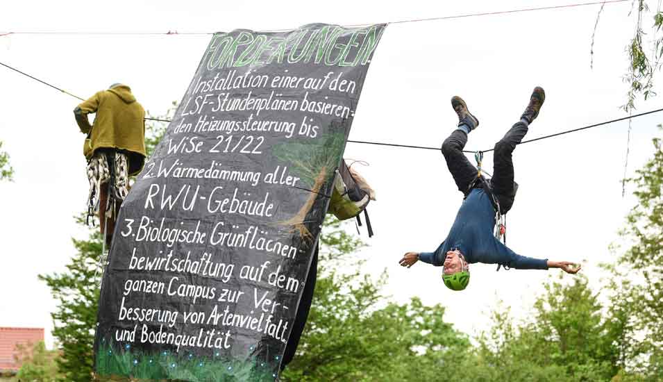 Professor Wolfgang Ertel hängt an der Hochschule Ravensburg-Weingarten an einem Seil neben einem Transparent mit Forderungen