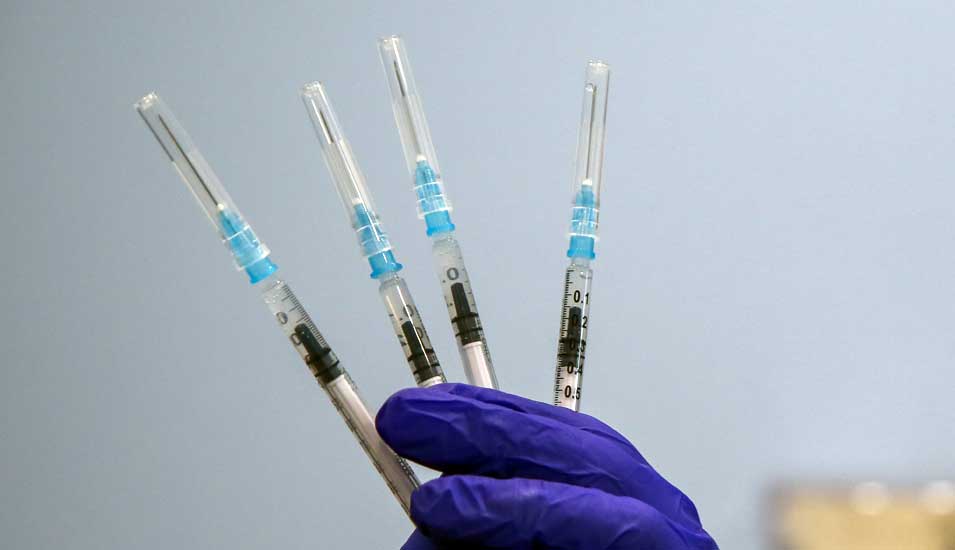 Hand in medizinischem Handschuh hält vier Spritzen mit Impfstoff