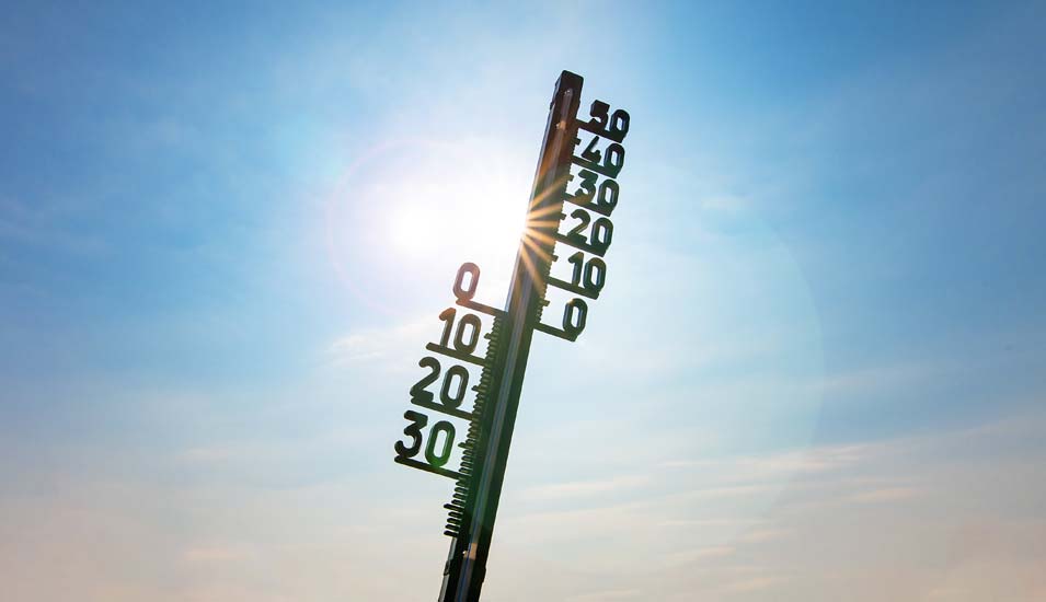 analoges Thermometer mit Kapillarröhrchen und freistehenden Gradzahlen vor einem blauen Himmel mit Sonnenschein