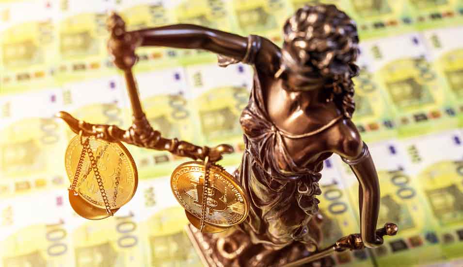 Zwei Bitcoin Gold Münzen auf der Waage einer Lady Justice Statue vor mehreren Hundert Euro Geldscheinen