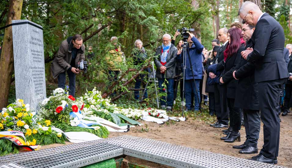 Anwesende auf dem Waldfriedhof Dahlem gedenken bei der Trauerfeier zur Bestattung der Knochen den Opfern.