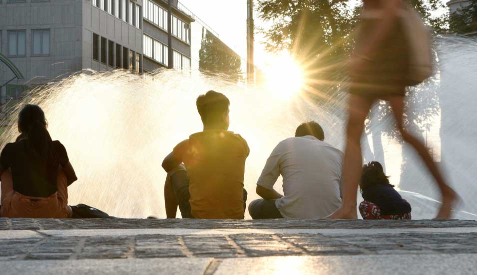 Menschen sitzen im Sommer bei Sonnenuntergang am Münchner Stachusbrunnen