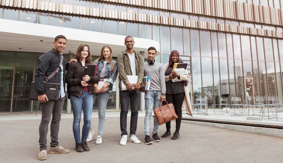 Sechs lachende Studierende mit und ohne Kopftuch vor einem Universitäts-Gebäude